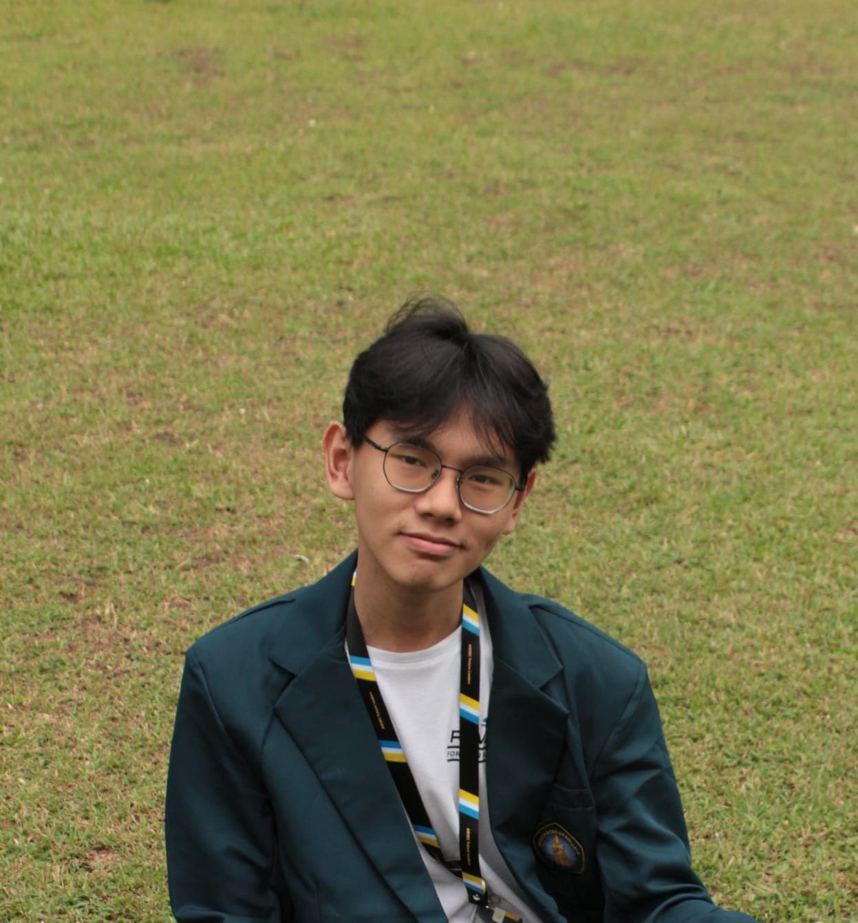 Richard in a university blazer seated on a grassy field
